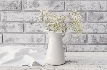 Vase with beautiful gypsophila flowers on table near brick wall