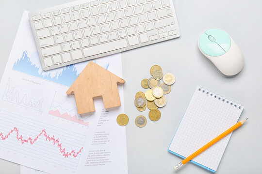 Wooden house with coins, diagrams and computer keyboard on light background