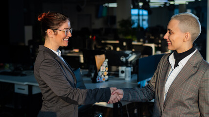 Two young business women shake hands at work. The office staff made a deal