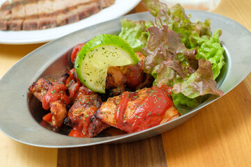 木のテーブルに置かれた鉄の皿に乗った美味しそうなジャークチキンとスライスされたライムとレタス