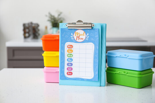 Stack of containers with healthy food and clipboard with meal plan on table in kitchen