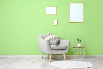 Grey armchair with table and blank frames hanging on green wall