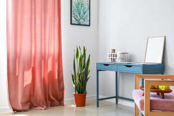 Blue table with blank frame, basket, vases and laptop near light wall in room