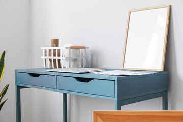 Blue table with blank frame, basket, vases and laptop near light wall