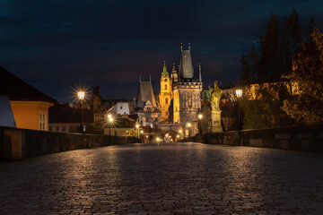 Fototapeta na wymiar .old cobbled sidewalk with paving Charles Bridge in the center of Prague and in the background the old bridge tower at night in the Czech Republic and the light from street lighting