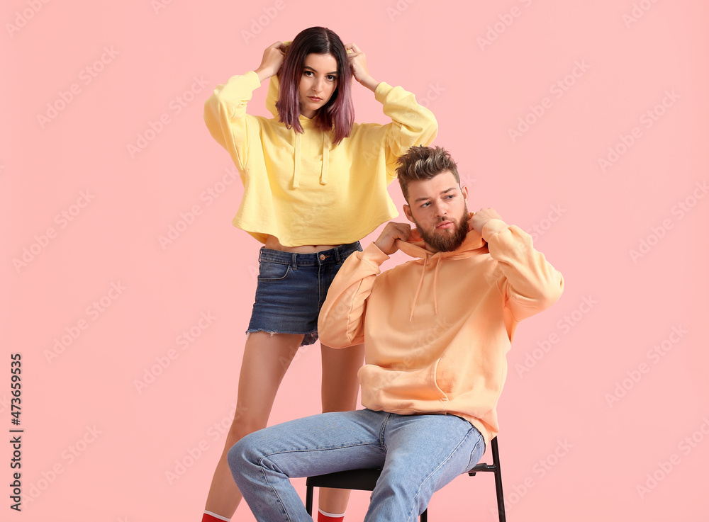 Wall mural Cool young couple in hoodies on color background