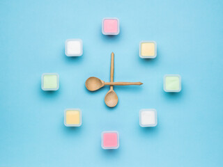 A clock made of plastic cups with yogurt and wooden spoon-shaped hands. The concept of healthy eating. Flat lay.