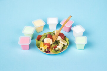 A wooden spoon in a bowl with fruit salad and cups with multicolored yogurt.