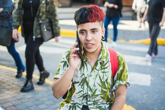 Latino queer man talking on the phone on busy street
