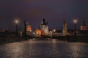 Pavement on Charles Bridge and silhouette of a homeless man and an old stone tower and light from lamps in the background in the center of Prague 2021