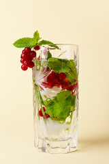 Glass of water with mint and red currant on color background