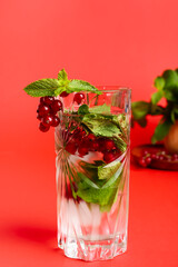 Glass of cold water with mint and red currant on red background
