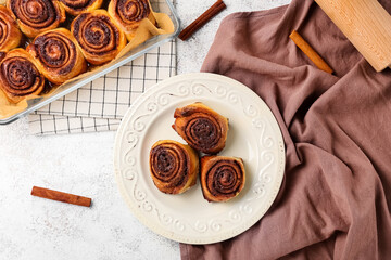 Baking dish and plate with tasty cinnamon rolls on light background