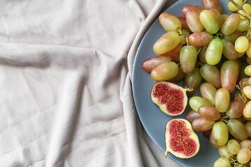 Plate with ripe grapes and fig on fabric background, closeup