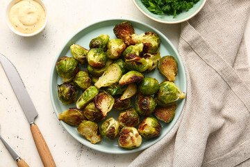 Plate with tasty roasted Brussels cabbage, greens and sauce on light background