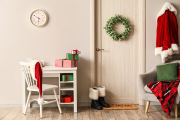 Workplace with gift boxes, door with Christmas wreath and Santa Claus costume near white wall