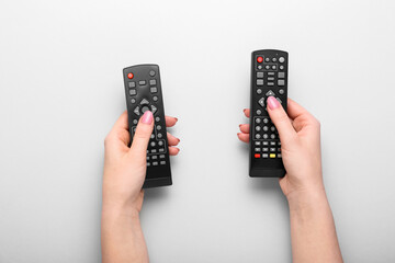 Female hands with TV remote controllers on grey background