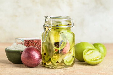 Jar with canned green tomatoes and fresh vegetables on table