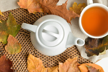 Tea pot, cup of hot beverage and autumn leaves on table