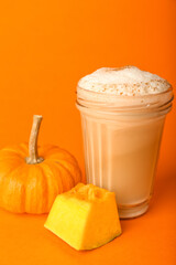 Glass of tasty pumpkin latte on orange background