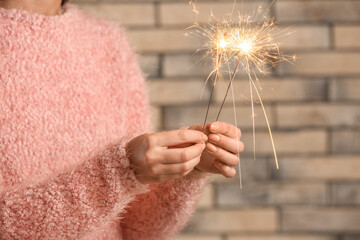 Woman in pink sweater holding Christmas sparklers on brick background, closeup
