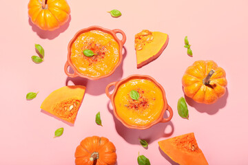 Pots with tasty pumpkin cream soup on pink background