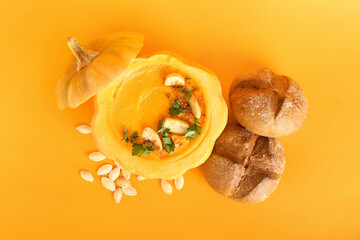 Delicious cream soup served in pumpkin with seeds and buns on orange background