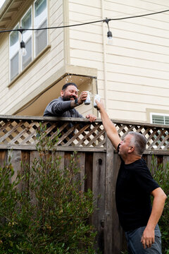 Two neighbors sharing beers over a fence 