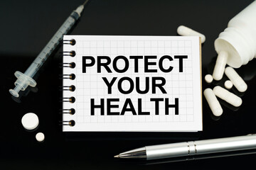 On the black surface are pills, a syringe and a notebook with the inscription - PROTECT YOUR HEALTH