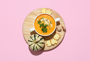 Pot with delicious pumpkin cream soup and croutons on pink background