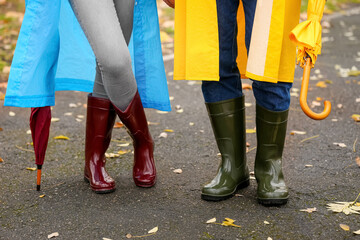 Couple wearing gumboots and raincoats in park on autumn day