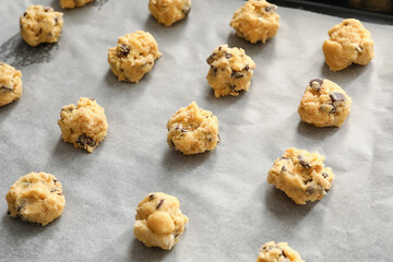 Uncooked cookies with chocolate chips on baking tray, closeup