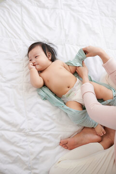 Adorable baby girl lying on bed while her mother changing his clothes before bedtime.