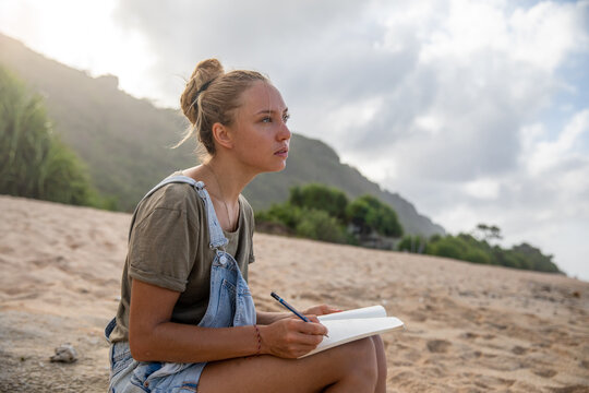 Woman sitting on sand writing in her notebook