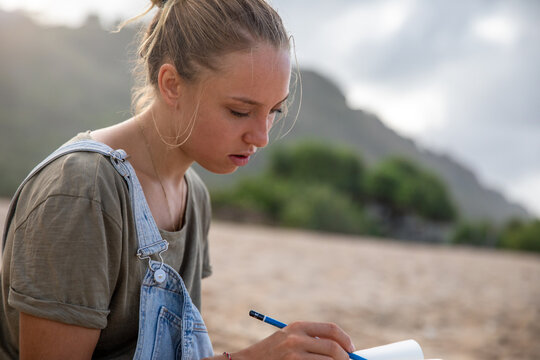 Student casually writing in notebook at beach