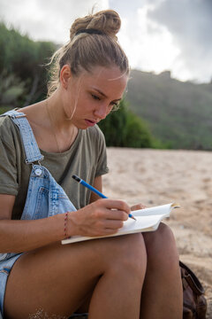Student sitting at the beach writing in notebook