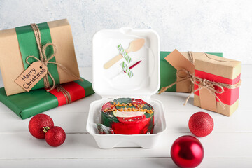 Plastic lunch box with Christmas bento cake, gifts and balls on light wooden background
