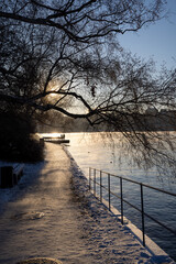 People walking on a walking path at Stockholm bay on freezing winter day with steaming water, birch...