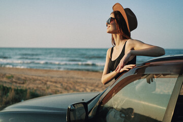 cheerful woman in sunglasses and a hat on the ocean near the car