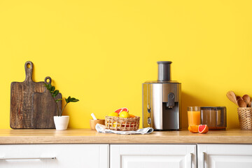 Modern juicer with fresh citrus fruits and glass of juice on table in kitchen