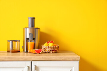 Modern juicer with fresh citrus fruits and glass of juice on table in kitchen