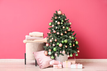Beautiful Christmas tree with gifts, pouf and pillow near pink wall