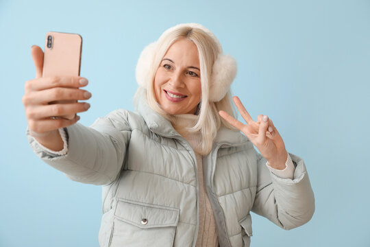 Mature Woman In Winter Clothes Taking Selfie On Color Background