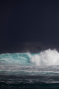 Stormy dark sky behind a big blue wave lite by the sunlight