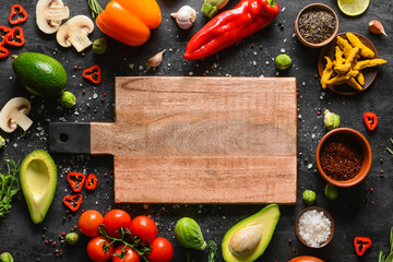 Wooden cutting board with tasty food and spices on dark background