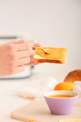 Woman spreading tasty tangerine jam onto toast at table in kitchen, closeup