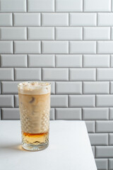 Modern iced latte with caramel syrup on white tile background