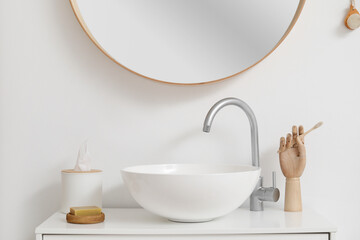 Modern sink with soap, wooden hand and tissue box near light wall