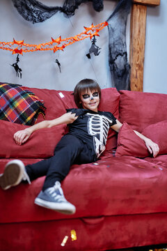Happy little boy in costume resting on couch at home