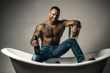 Sexy smiling man sit on bathtub in bathroom, men holiday with champagne. Celebrating christmas or birthday. Private sex party. - obrazy, fototapety, plakaty